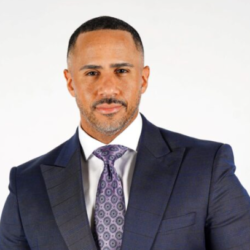 A man in a suit and tie standing up against a white wall.